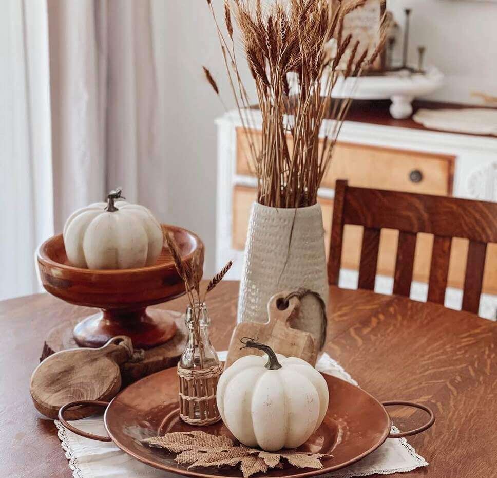 Neutral fall centerpiece on a kitchen counter with dried lunaria branches in a textured vase, a candle in a wicker stand, and a ceramic leaf dish on a tray.